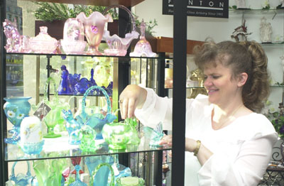 Michelle Dieringer arranges some Fenton glass on a shelf in her store, Etcetera, on Main Street in Celina. The shop had been known as Rankin's for more than 40 years, but its name was changed recently after a contest to rename it was held.<br>dailystandard.com