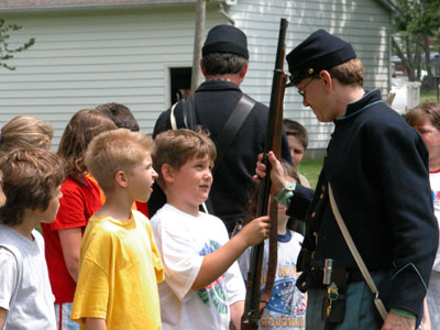 A Civil War re-enactor, dressed in full uniform, hands his musket to a St. Marys fifth-grader to check out at one of nine learning stations outside East elementary school Friday.<br>dailystandard.com