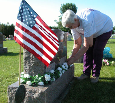 Ruth Ann Lennartz of Coldwater positions a spray of flowers around the grave marker of her husband in preparation of Memorial Day. Melvin A. Lennartz, a U.S. Army veteran of the Korean War, died of cancer in 1979 and is buried in St. Elizabeth Cemetery, Coldwater.<br>dailystandard.com