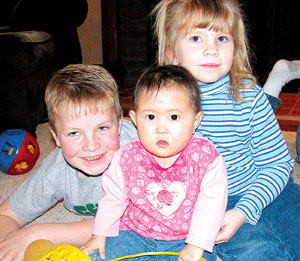 Andrew and Natalie Homan play with their new sister, 14-month-old Audrey, who was adopted from China and brought home earlier this month. Parents Ted and Allison Homan of rural Coldwater are shown below.<br>dailystandard.com