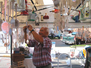 Douglas Millares of Union City, Ind., hangs a silver windchime in his stand along Fayette Street during Celina Lake Festival sidewalk sales this morning. Millares and wife, Kathy, offer silverware windchimes attached to antique looking items such as pitchers and teapots.<br>dailystandard.com