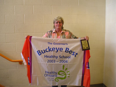 Coldwater Elementary School Principal Molly Hay displays the flag and plaque the school received recently from the Governor's Buckeye Best Healthy Schools Awards Program 2003-04.<br>dailystandard.com