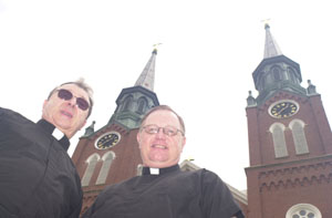 The spires of St. Augustine Catholic Church in Minster loom in the background as the Rev. Louis Schmit, left, prepares to turn over pastoral duties to the Rev. Rick Nieberding, the current associate pastor. Schmit is retiring June 30 after 43 years as a priest and military chaplain.<br></br>dailystandard.com