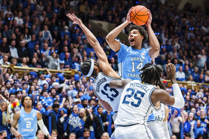 North Carolina forward Puff Johnson (14) looks to shoot while guarded by Duke guard Jacob Grandison (13) and forward Mark Mitchell (25) in the first half of an NCAA college basketball game on Saturday, Feb. 4, 2023, in Durham, N.C. (AP Photo/Jacob Kupferman)