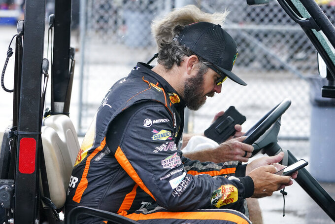 Driver Martin Truex Jr. looks at his phone as he rides in a golf cart after a NASCAR Cup Series auto race qualifying session Saturday, June 25, 2022, in Lebanon, Tenn. (AP Photo/Mark Humphrey)