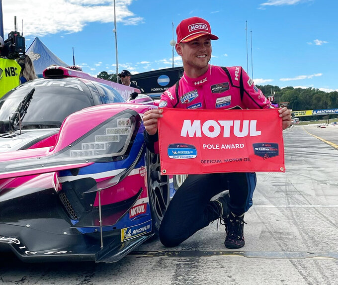 Tom Blomqvist, of Meyer Shank Racing, poses with flag after qualifying for the pole position, Friday, Sept. 30, 2022, in the IMSA sports cars season-ending Petit Le Mans auto race at Road Atlanta in Braselton, Ga. The team goes into Saturday's race second in the championship standings. Ensuing pictures show teammate Helio Castroneves congratulating Blomqvist, team owner Mike Shank and drivers Helio Castroneves and Oliver Jarvis watching Blomqvist qualify. (AP Photo/Jenna Fryer)